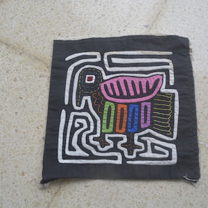 Könnte beinhalten: Schwarzer Stoff mit einem weißen gestickten Design eines Vogels mit rosa, orange, blauen und grünen Akzenten.