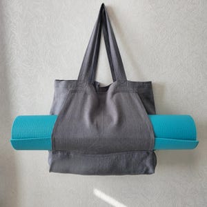 May include: A gray canvas tote bag with a teal yoga mat tucked inside. The bag has a wide opening and two long handles.