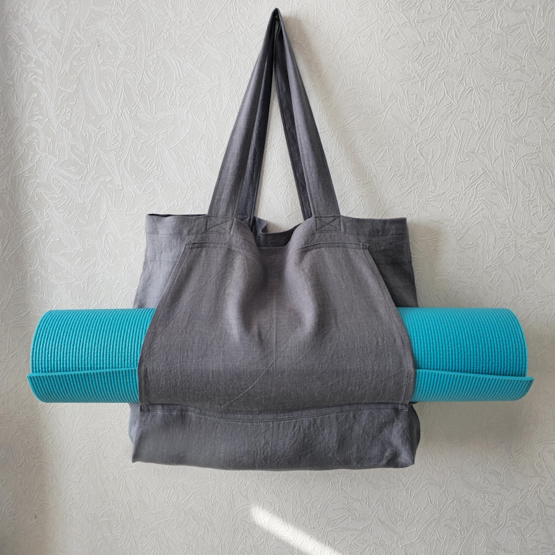 May include: A gray canvas tote bag with a teal yoga mat tucked inside. The bag has a wide opening and two long handles.