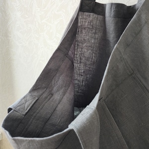 May include: A gray linen tote bag with a single strap. The bag is made of a thick, durable fabric and has a simple, classic design.