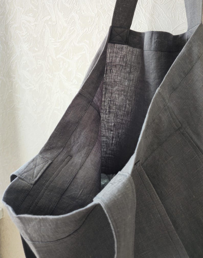 May include: A gray linen tote bag with a single strap. The bag is made of a thick, durable fabric and has a simple, classic design.