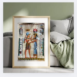 May include: Framed artwork depicting ancient Egyptian figures in vibrant colors. The artwork features detailed illustrations of two figures, adorned with traditional attire and headdresses, set against a backdrop of hieroglyphs. The frame is a light brown color.