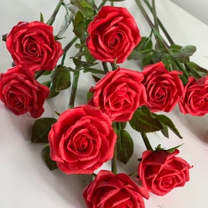 May include: A bouquet of ten red roses with green leaves and stems. The roses are made of a material that looks like clay.