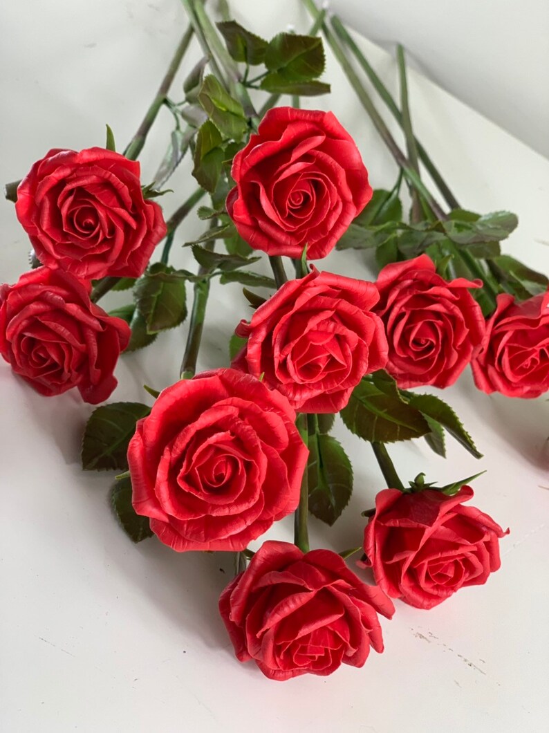 May include: A bouquet of ten red roses with green leaves and stems. The roses are made of a material that looks like clay.