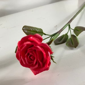 May include: A single red rose with green leaves on a white background.