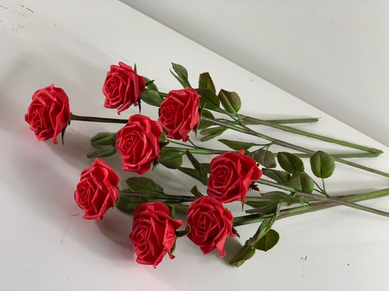 May include: A bouquet of eight red roses with green stems and leaves.
