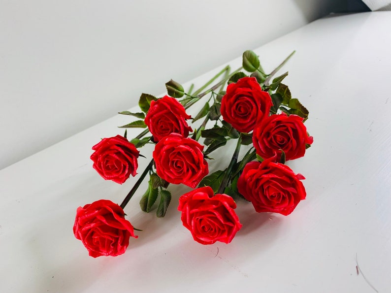 May include: A bouquet of eight red roses with green stems and leaves.