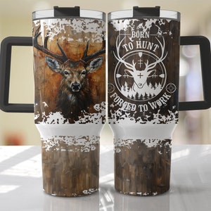 May include: A stainless steel travel mug with a black handle and lid. One side features a detailed deer portrait against a wood-grain background. The other side displays the text "BORN TO HUNT FORGED TO WORK" with a deer silhouette.