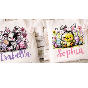May include: Two white canvas tote bags with personalised names, "Isabella" and "Sophia". Each bag features a cartoon animal surrounded by colourful Easter eggs and flowers. The left bag has a black and white cow with bunny ears, while the right bag has a yellow chick with bunny ears.