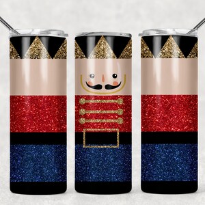 Op de afbeelding: Drie roestvrijstalen bekers met een glitterafwerking. De bekers zijn versierd met een Notenkraker-ontwerp. Het ontwerp heeft een rood, goud en blauw kleurenschema. De bekers zijn perfect voor het vasthouden van warme of koude dranken.