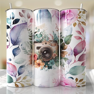 May include: Three stainless steel tumblers with a white background and floral designs. The center tumbler features a vintage camera with flowers surrounding it. The tumblers are perfect for holding hot or cold beverages.