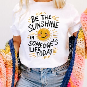 May include: White t-shirt with a black and yellow graphic that says "Be the sunshine in someone's life today". The graphic features a yellow sun with a smiling face.
