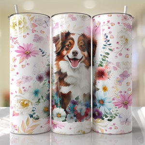 May include: A white tumbler with a floral pattern and a watercolor painting of an Australian Shepherd dog. The dog is brown and white with a pink nose and tongue.