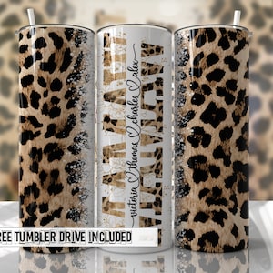 May include: A white tumbler with a leopard print design and the text "Mama" in gold glitter lettering. The text "Victoria Thomas Charles Alex" is written in cursive on the side of the tumbler.