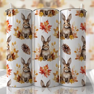 May include: Three white stainless steel tumblers with a fall-themed design. The design features brown rabbits, orange and yellow leaves, and brown pine cones.
