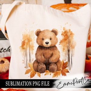 May include: A brown bear cub sitting on a bed of autumn leaves. The bear is surrounded by watercolor trees with brown trunks and orange leaves. The background is a white canvas tote bag with the text "SUBLIMATION PNG FILE" and "EmmePrintCo" at the bottom.