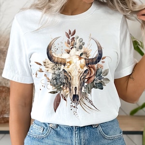 May include: White t-shirt with a floral design featuring a brown and white bull skull. The flowers are in shades of brown, white, and green.