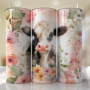 K&ouml;nnte beinhalten: Ein wei&szlig;er Becher mit einer schwarz-wei&szlig;en Kuh mit rosa Nase und braunen Augen, umgeben von rosa und wei&szlig;en Aquarellblumen.