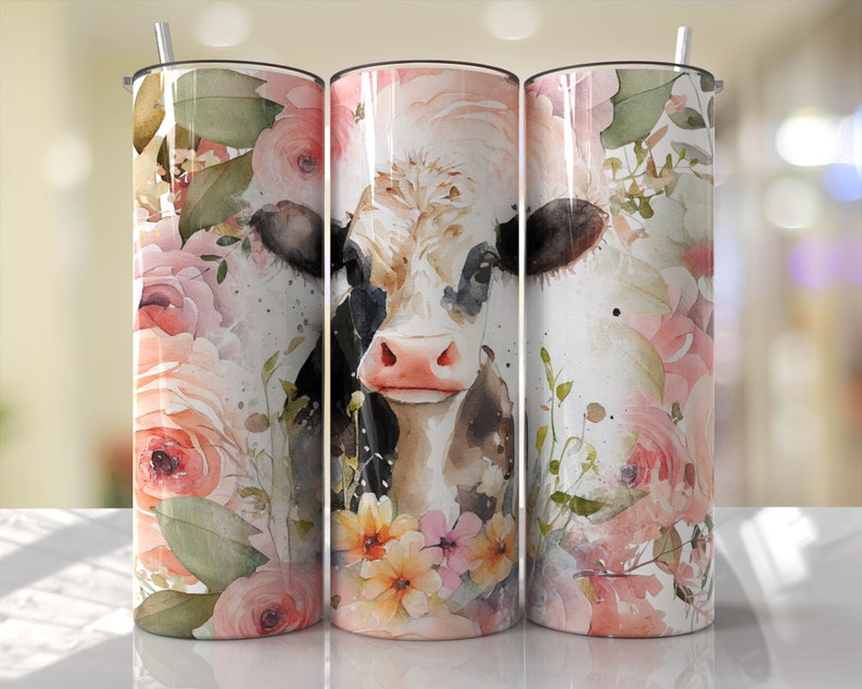 K&ouml;nnte beinhalten: Ein wei&szlig;er Becher mit einer schwarz-wei&szlig;en Kuh mit rosa Nase und braunen Augen, umgeben von rosa und wei&szlig;en Aquarellblumen.