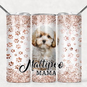 Puede incluir: Un vaso de acero inoxidable blanco con un diseño de purpurina dorada rosa y huellas de patas. El vaso tiene un perro blanco con ojos marrones y una nariz rosa en la parte delantera. El texto "Maltipoo Mama" está impreso en el vaso.