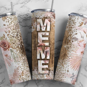 May include: Three stainless steel tumblers with a wood grain background and floral designs. The center tumbler has the word "MEME" printed on it.
