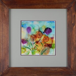 May include: A framed abstract watercolor painting of a field of flowers in shades of purple, orange, and yellow. The flowers are painted in a loose, expressive style, and the background is a soft blue.