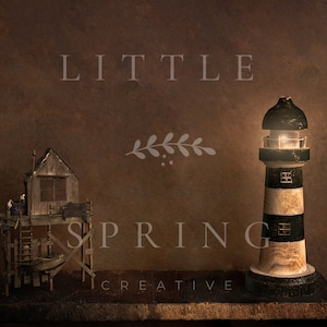 May include: A miniature lighthouse and a rustic wooden structure are displayed on a dark brown surface. The lighthouse is black, white, and beige, with a glowing light. The wooden structure resembles a small house on stilts. The text "LITTLE SPRING CREATIVE" is visible.