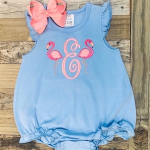May include: Light blue baby onesie with a pink flamingo and a pink letter E embroidered on the front. The onesie has ruffles on the sleeves and around the bottom.