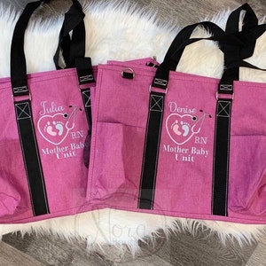 May include: Two pink tote bags with black straps and pockets. The bags are embroidered with the names "Julia" and "Denise", a heart with footprints, and the text "RN Mother Baby Unit".