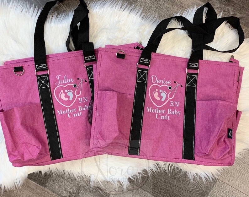 May include: Two pink tote bags with black straps and pockets. The bags are embroidered with the names "Julia" and "Denise", a heart with footprints, and the text "RN Mother Baby Unit".
