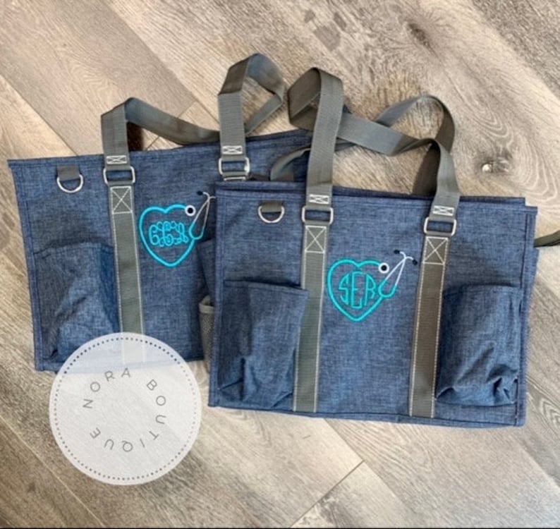 May include: Two blue tote bags with gray straps and a heart-shaped monogram with a stethoscope. The monogram on the left bag says "GGG" and the monogram on the right bag says "SEB".