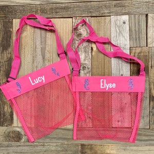 May include: Two pink mesh bags with adjustable straps. Each bag has a pink fabric band with a seahorse design and the names "Lucy" and "Elyse" written in white.