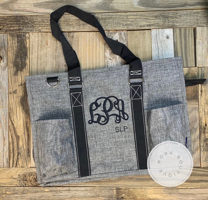 May include: A gray tote bag with black straps and a monogrammed design. The monogram is "SLP" in black embroidery. The bag has a zippered closure and a small pocket on the front.
