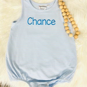 Op de afbeelding: Een lichtblauwe en wit gestreepte mouwloze baby romper met de naam "Chance" geborduurd in blauw op de voorkant.