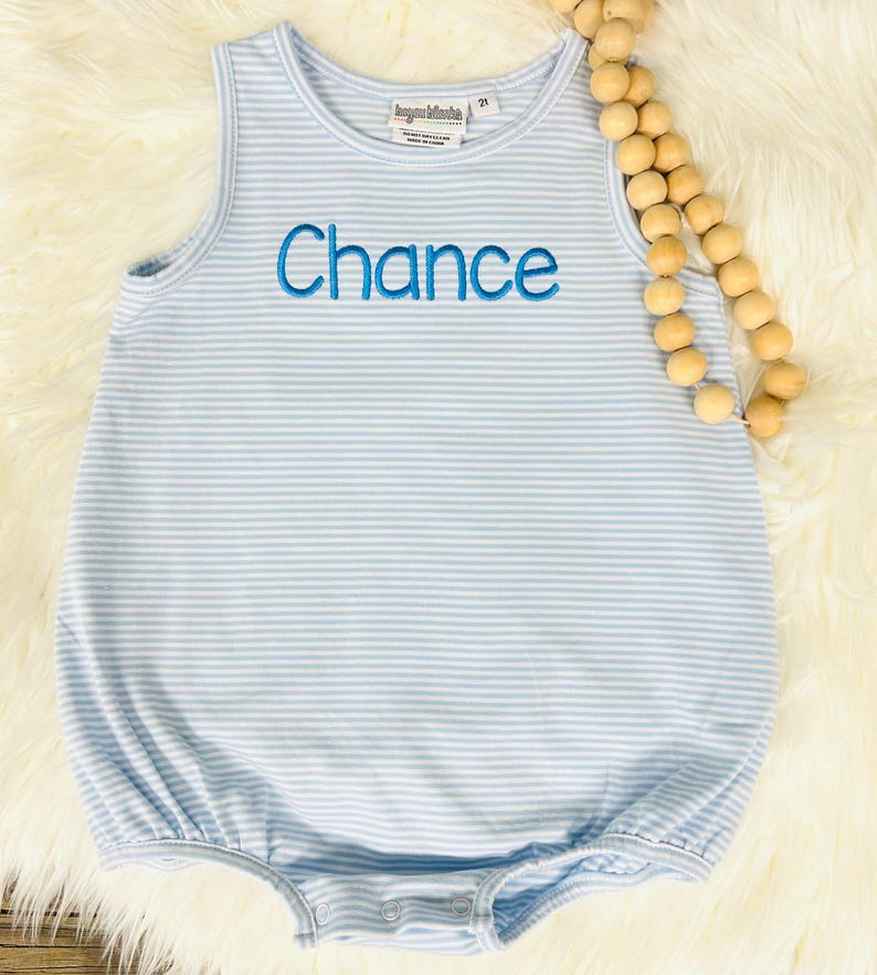 Op de afbeelding: Een lichtblauwe en wit gestreepte mouwloze baby romper met de naam "Chance" geborduurd in blauw op de voorkant.