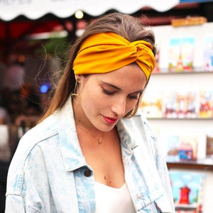 May include: A woman wearing a mustard yellow turban headband. She is wearing a light blue denim jacket over a white shirt.
