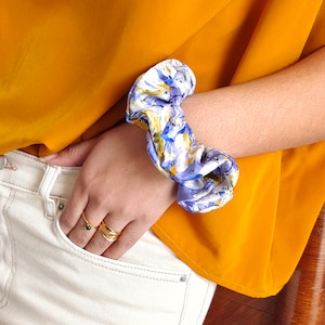 Puede incluir: Un scrunchie de estampado floral blanco y morado sobre fondo amarillo.