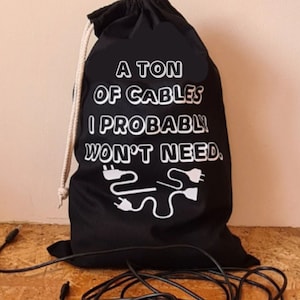 May include: A black drawstring bag with the text "A Ton of Cables I Probably Won't Need." The bag is filled with black electrical cords.