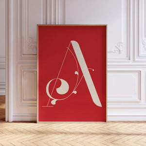 Op de afbeelding: Een ingelijst print met een witte gestileerde letter A op een rode achtergrond. De letter A is versierd met een gestileerd bloemmotief.