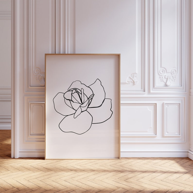 Puede incluir: Un dibujo en blanco y negro de una sola rosa en un marco dorado contra una pared blanca.
