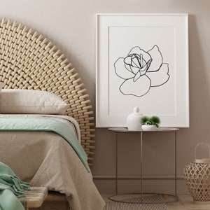 Puede incluir: Un dibujo en blanco y negro de una rosa en un marco blanco sobre una pared marr&oacute;n claro. El marco est&aacute; sobre una mesa redonda peque&ntilde;a con un jarr&oacute;n de cer&aacute;mica blanco y una peque&ntilde;a planta verde.