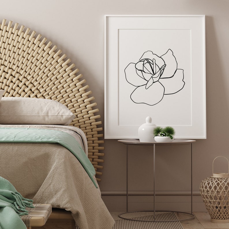 Puede incluir: Un dibujo en blanco y negro de una rosa en un marco blanco sobre una pared marr&oacute;n claro. El marco est&aacute; sobre una mesa redonda peque&ntilde;a con un jarr&oacute;n de cer&aacute;mica blanco y una peque&ntilde;a planta verde.