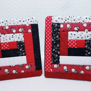 Puede incluir: Dos agarraderas de olla acolchadas de color rojo, negro y blanco con un patrón de muñeco de nieve. Las agarraderas están hechas de recortes de tela y tienen un diseño de patchwork.