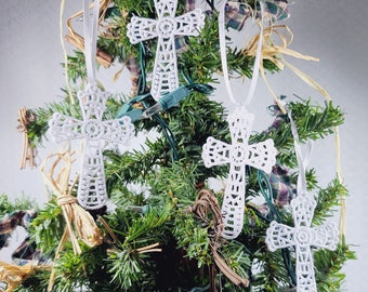 Op de afbeelding: Vijf witte gehaakte kruisversieringen die aan een groene kerstboom hangen met bruin en geruit lint.