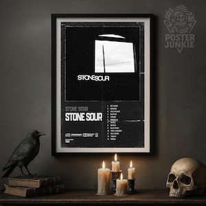 May include: A framed black and white poster featuring the band Stone Sour. The poster has the band's name and song titles listed. A black raven statue, books, candles, and a skull are on a wooden surface in front of a dark wall.