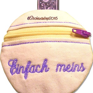 May include: A small, white fabric pouch with a purple zipper and a purple embroidered phrase that reads "einfach meins". The pouch has a purple ribbon loop at the top.