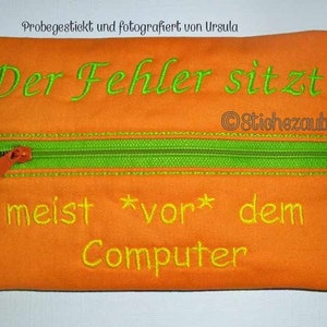 May include: Orange zippered pouch with green zipper and yellow stitching. The pouch has the text "Der Fehler sitzt meist *vor* dem Computer" embroidered on it.