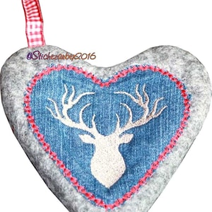 Könnte beinhalten: Ein grauer Filz-Herz-Anhänger mit einem blauen Jeans-Herz im Inneren. Das Jeans-Herz hat einen weißen gestickten Hirschkopf mit Geweih. Der Anhänger hat ein rot-weißes Gingham-Band, das oben befestigt ist.
