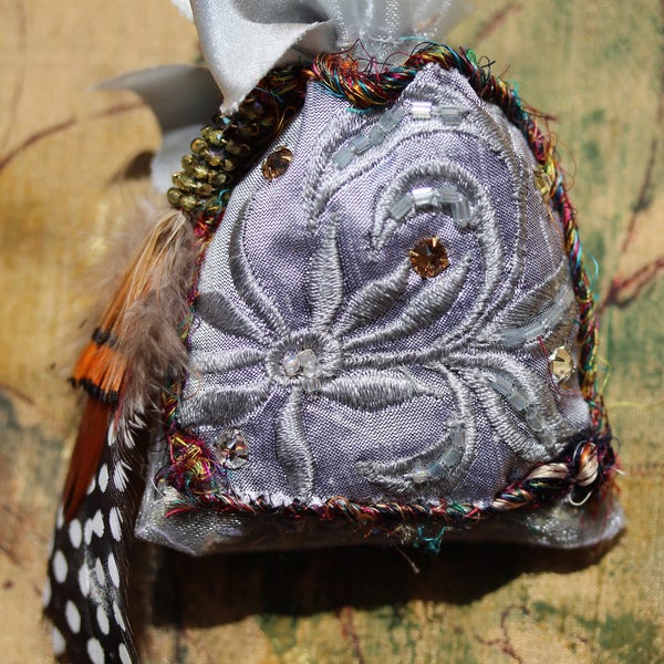 Lavender sachet embellished with beaded silver silk fabric, edged in recycled Nepalese silk cording, with swarovski crystals and feathers.