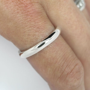 May include: A simple, polished silver band ring worn on a finger.